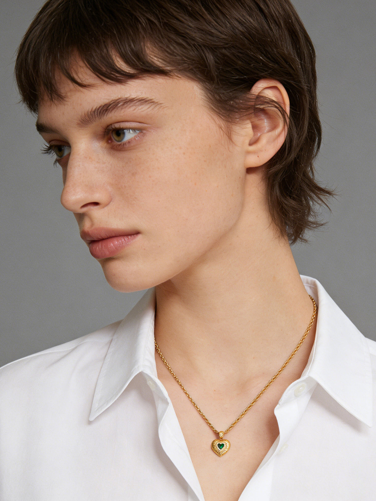 Emerald Heart Pendant Necklace in gold with a green heart, shown on a model facing left