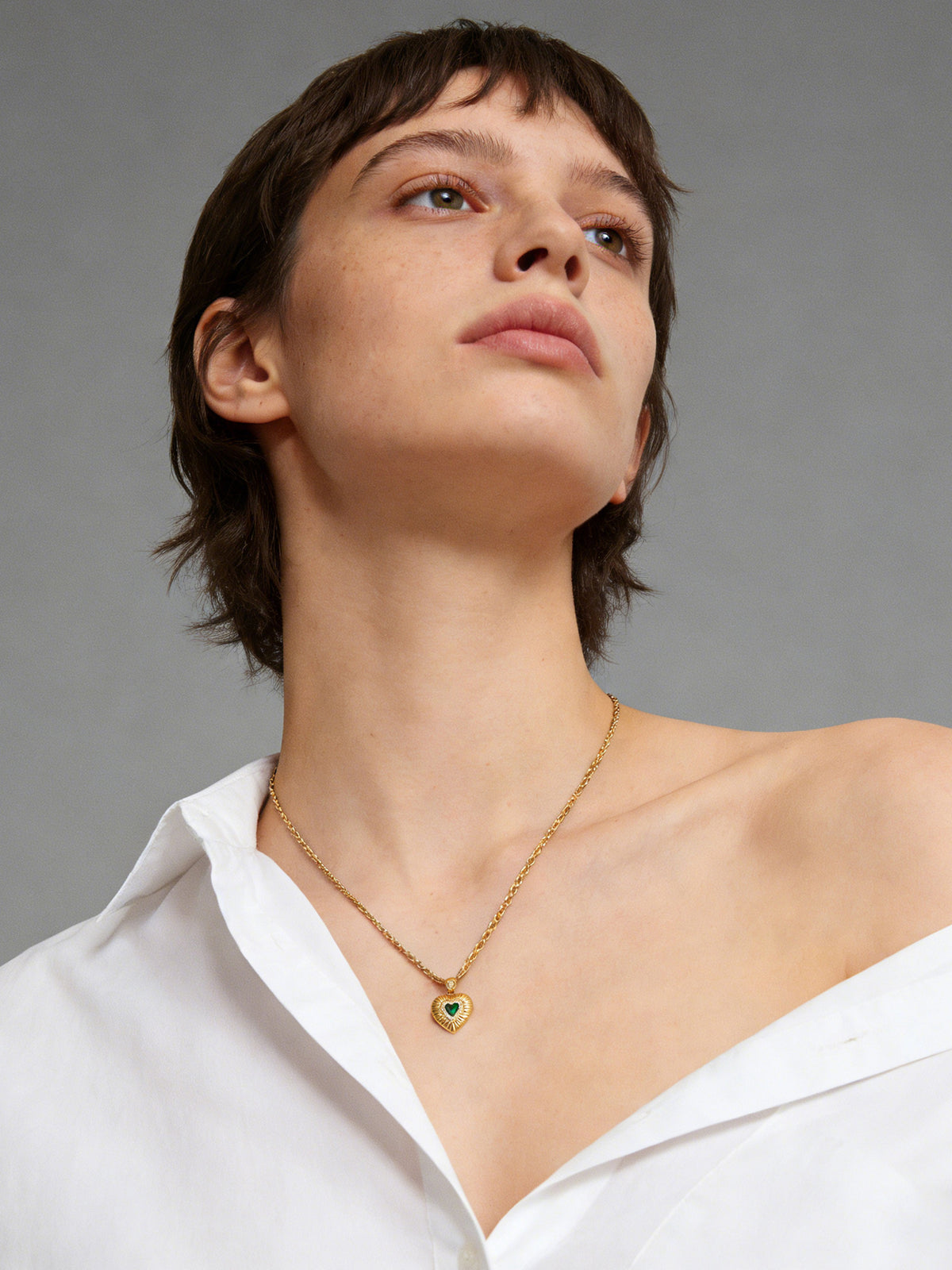 Emerald Heart Pendant Necklace in gold with a green heart, shown on a model looking up