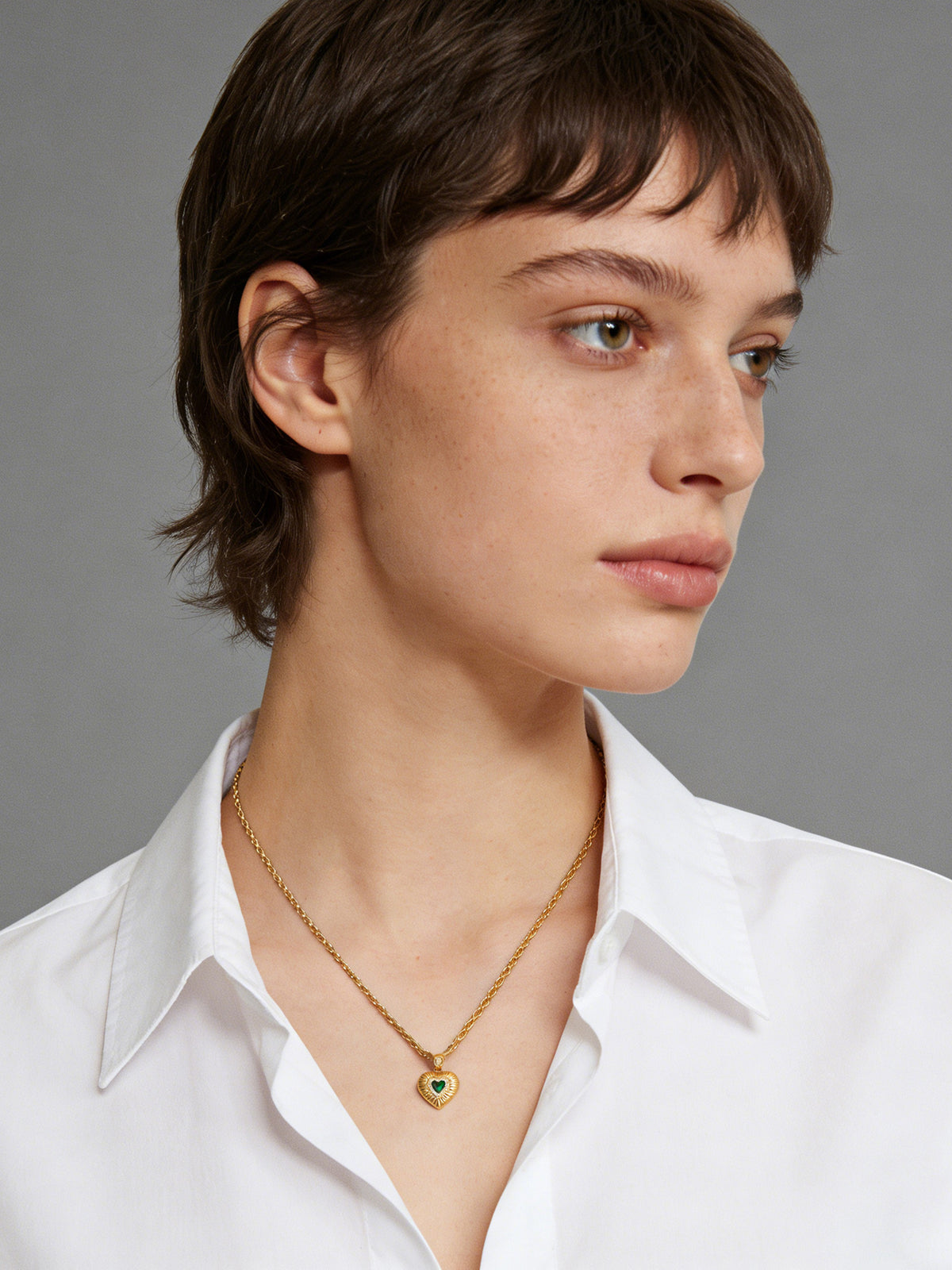 Emerald Heart Pendant Necklace in gold with a green heart, shown on a model facing right