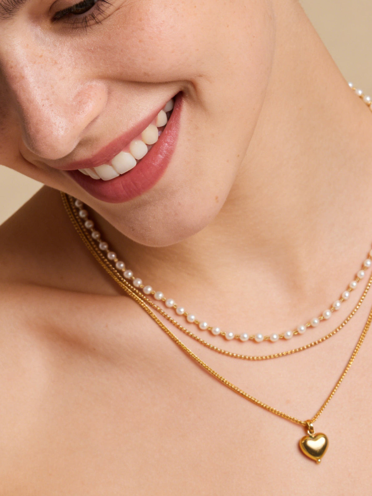 Layered Heart Pendant Necklace in gold with faux pearls, shown on a model, close-up three-quarter view