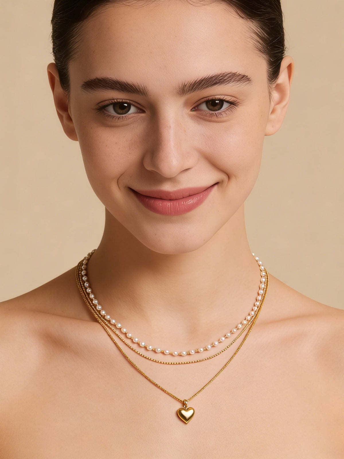 Layered Heart Pendant Necklace in gold with faux pearls, shown on a model smiling, front view