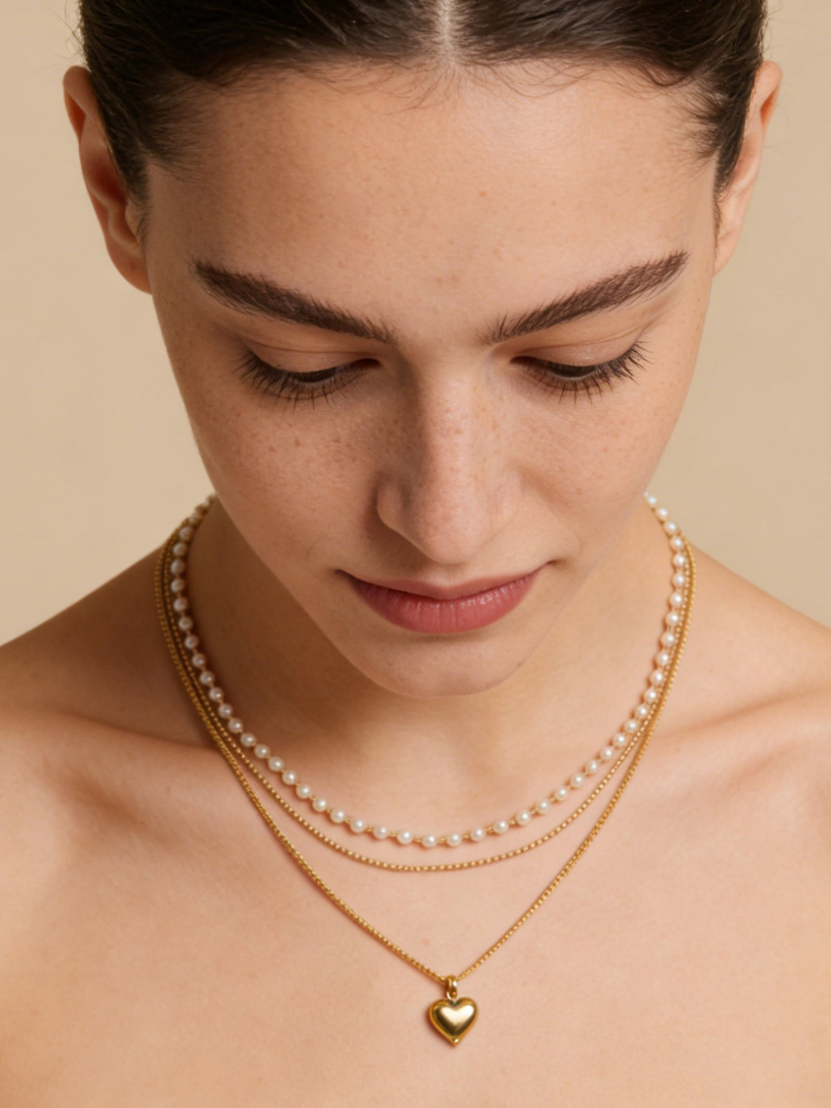 Layered Heart Pendant Necklace in gold with faux pearls, shown on a model looking down