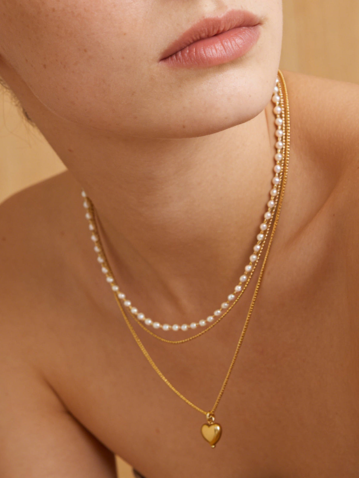 Layered Heart Pendant Necklace in gold with faux pearls, shown on a model, warm close-up view