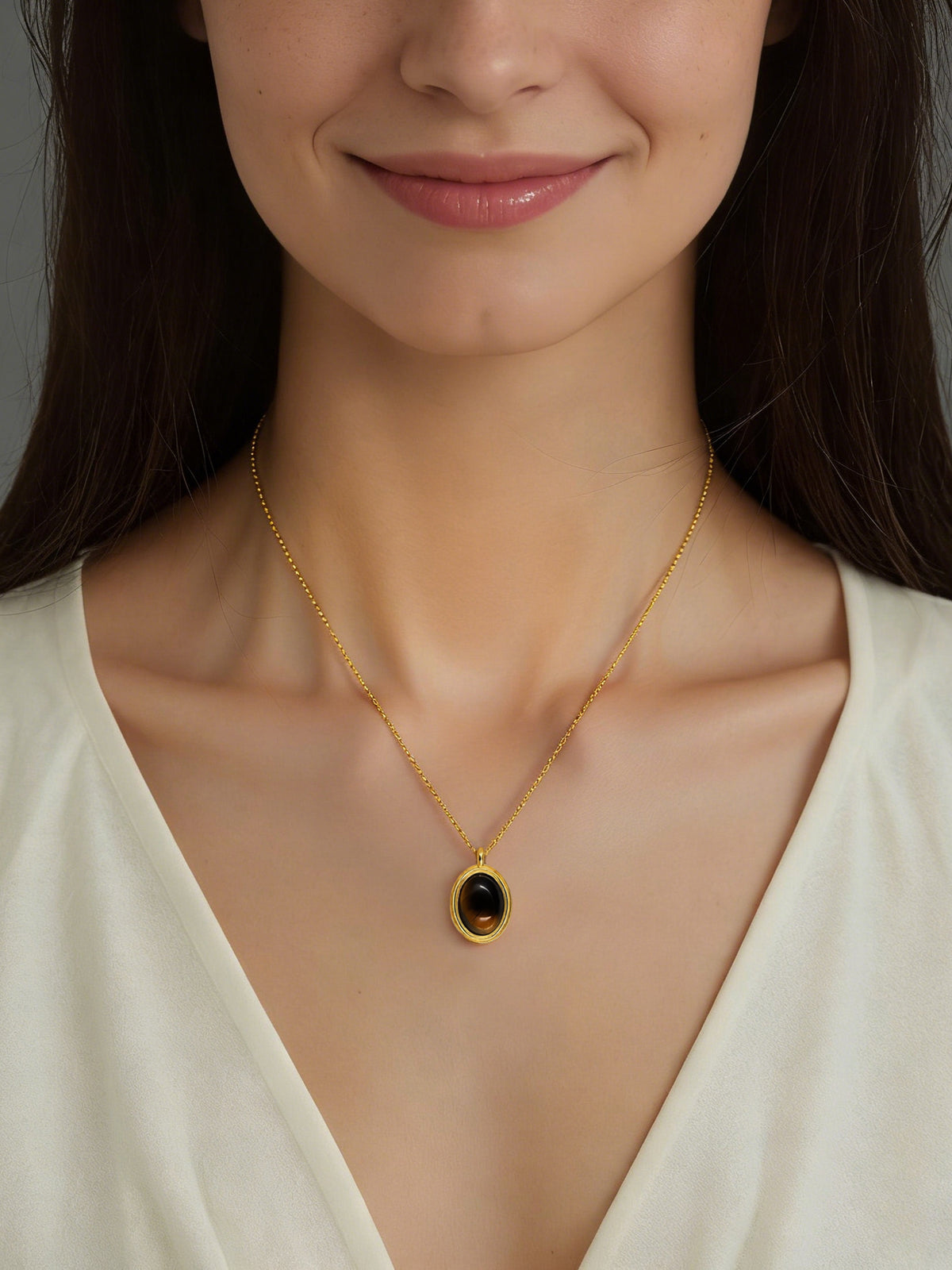 Oval Glow Pendant Necklace in gold with a brown stone, shown on a model smiling, front view