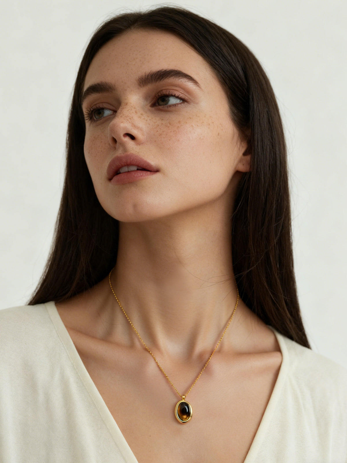 Oval Glow Pendant Necklace in gold with a brown stone, shown on a model looking up, front view