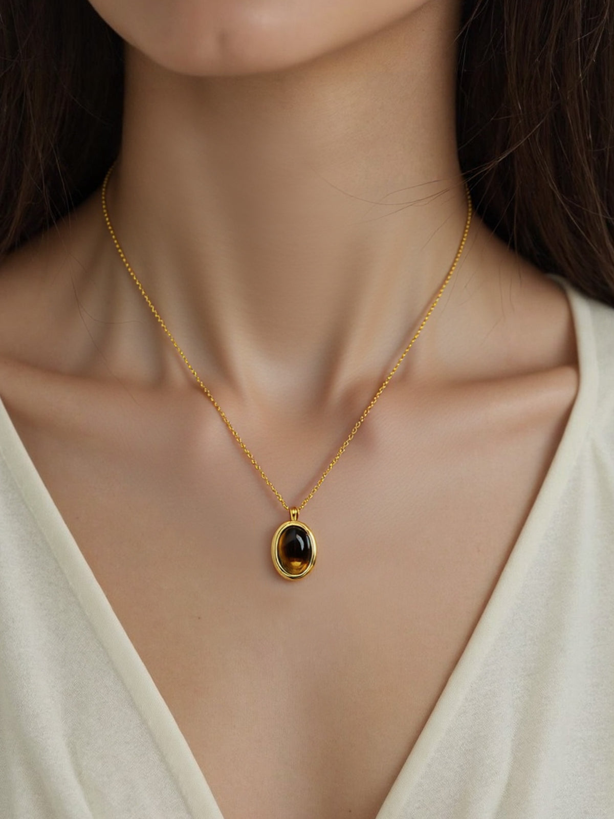 Oval Glow Pendant Necklace in gold with a brown stone, shown on a model, neck close-up