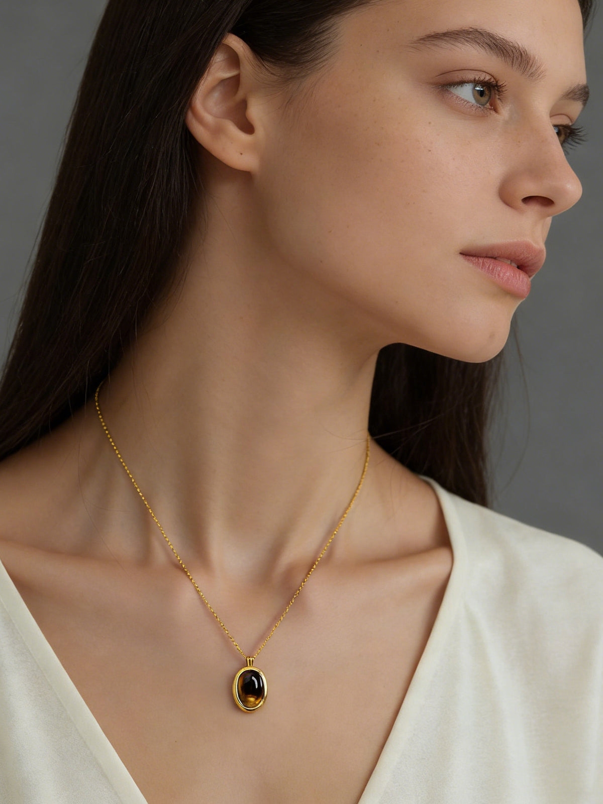 Oval Glow Pendant Necklace in gold with a brown stone, shown on a model, right profile view