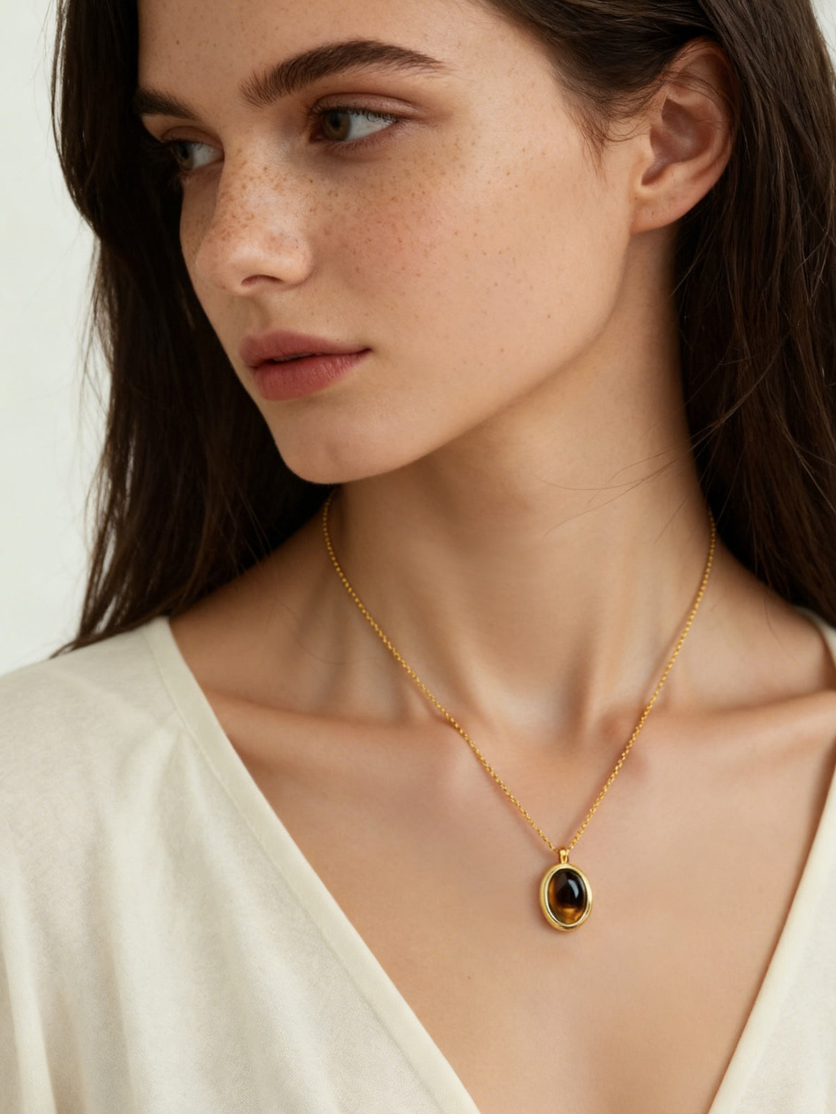 Oval Glow Pendant Necklace in gold with a brown stone, shown on a model, three-quarter view